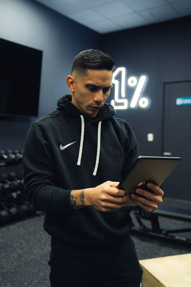 Diego Carquín revisando una programación en su tablet bajo el letrero de neón 1%.